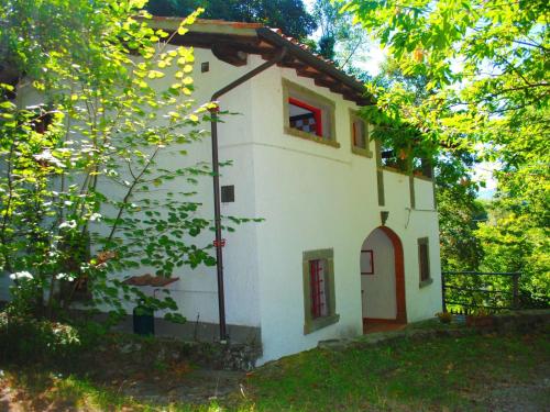 mały biały dom z czerwonym oknem i drzewami w obiekcie Belvilla by OYO La Loggia w mieście San Marcello Pistoiese