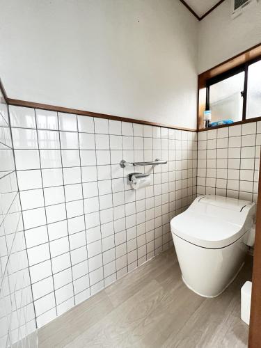 a white tiled bathroom with a toilet and a window at 8 Guests Entire Private House in Gifu