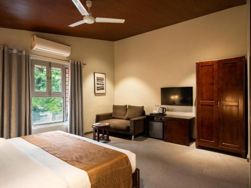 a bedroom with a bed and a chair and a television at Hotel Marigold Mount Abu - With Swimming Pool in Mount Ābu
