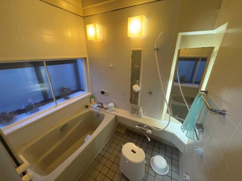 a bathroom with a tub and a toilet and a sink at ゲストハウス あめりか和 in Namerikawa