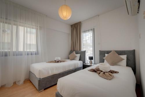 two beds in a room with white walls and windows at Aphrodite Limassol Apartment in Limassol