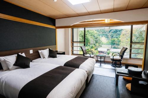two beds in a hotel room with a large window at LiVEMAX RESORT Okudogo in Matsuyama
