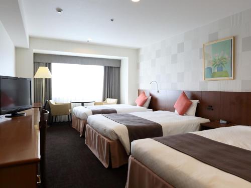 a hotel room with three beds and a flat screen tv at Loisir Hotel Toyohashi in Toyohashi