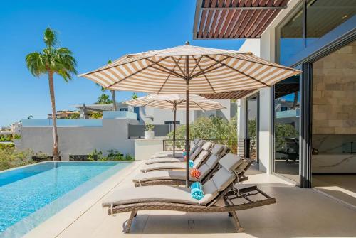 a group of chairs under an umbrella next to a swimming pool at Villa Real para 12 personas con piscina privada in Cabo San Lucas
