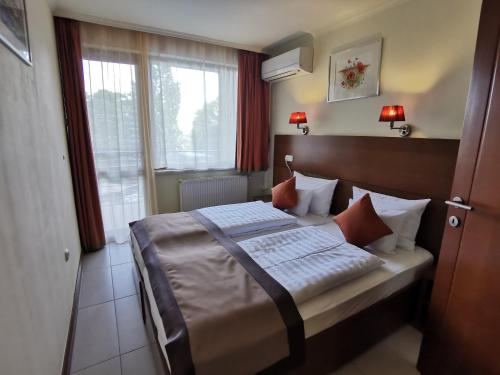 ein Schlafzimmer mit einem Bett in einem Zimmer mit Fenstern in der Unterkunft Hotel Villa Pax in Balatonalmádi
