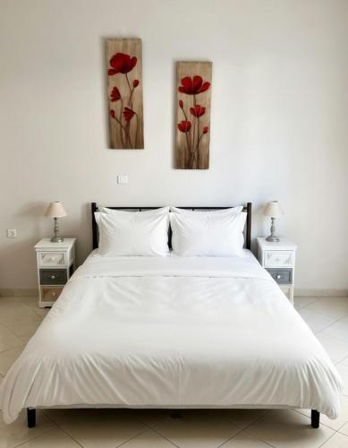 a bedroom with a white bed with three paintings on the wall at Mairi’s Apartment in Nea Artaki