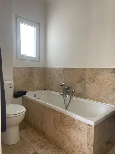 a bathroom with a tub and a toilet and a window at La Jolie Dauphine Guest House in Franschhoek