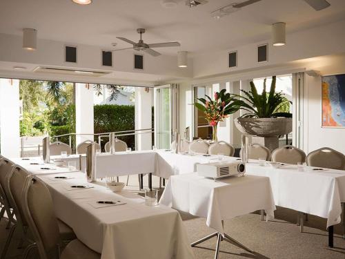 a dining room with white tables and chairs at Peppers Beach Club in Port Douglas