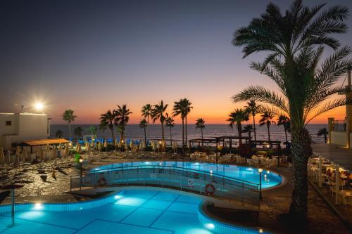 a pool with palm trees and the ocean at night at Kefalos Beach Tourist Village in Paphos
