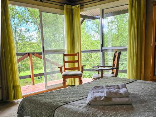 a bedroom with a bed and two chairs and a large window at Posada Quellen in Villa General Belgrano