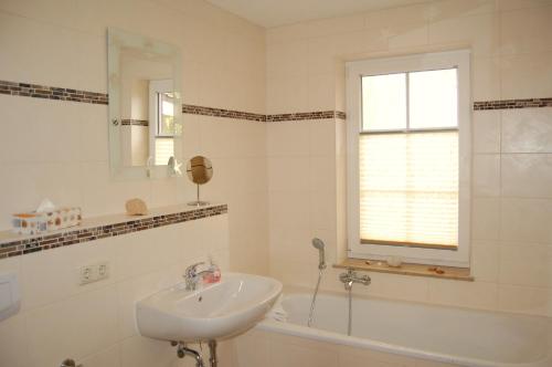 a white bathroom with a sink and a tub and a window at Hus an de Küst 02 in Ahrenshoop