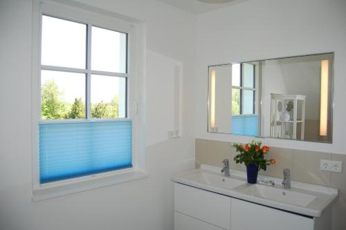 a white bathroom with a sink and two windows at Min Droom in Wustrow