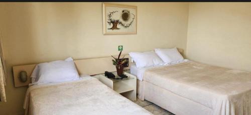 two beds in a room with white sheets at Quarto Hotel Palhano londrina in Londrina