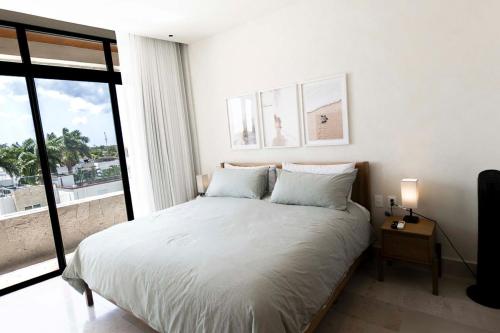 a white bedroom with a bed and a large window at QUEEN ANGEL condo in Cozumel