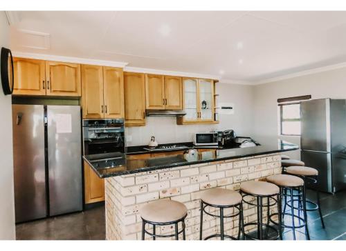a kitchen with wooden cabinets and a counter with bar stools at Aloe Corner, Cathkin Estates by Euphoric Leisure in Ardmore