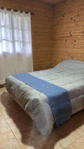 a bed in a wooden room with a window at Cabaña la Relajación in San Miguel del Monte