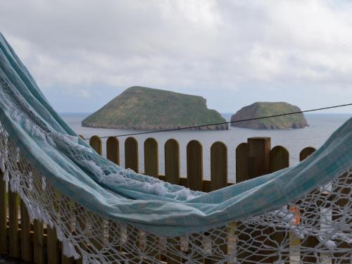a hammock on the beach with two islands in the water at Casinha de Muda da Feteira in Angra do Heroísmo