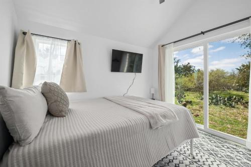 a white bedroom with a bed and a large window at Twilight Ranch Tiny Homes - pet friendly & hill country views in Fredericksburg