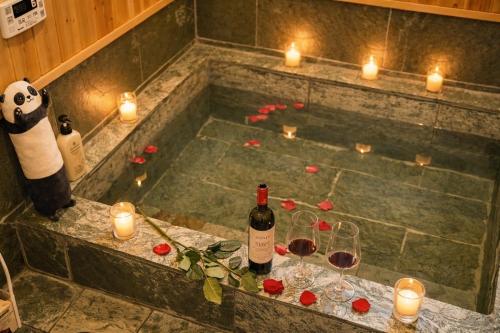 a bath tub with candles and wine bottles and glasses at 天然温泉付別荘Green House in Shirahama