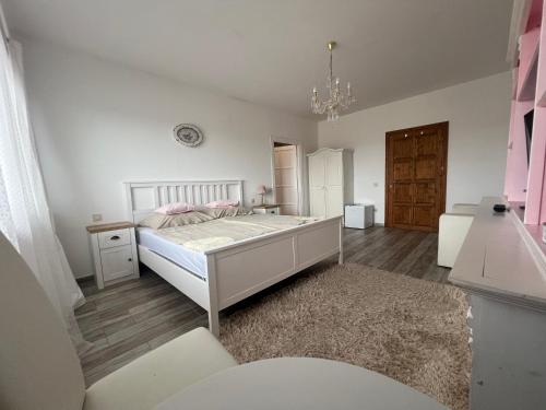 a white bedroom with a bed and a chandelier at Gold Horse Vendégház in Szilvásvárad