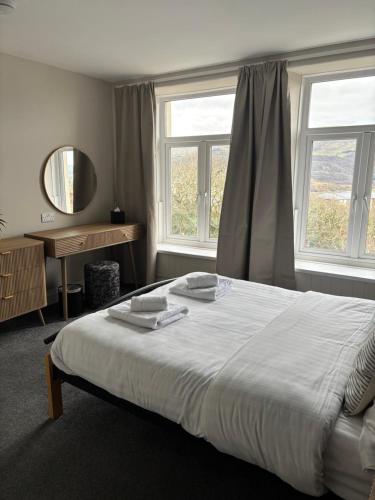 a bedroom with a large bed and two windows at Bryn Melyn Apartments in Barmouth