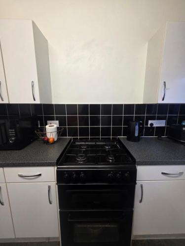 a kitchen with a black stove and white cabinets at Private Cosy Double Bedroom, extremely close to city centre in Manchester