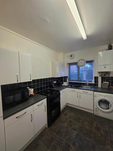 a kitchen with white cabinets and a black stove at Private Cosy Double Bedroom, extremely close to city centre in Manchester