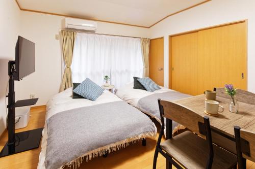 two beds in a room with a table and a window at 10 minutes by train to Nagoya Station! Kominka guest house in Nagoya
