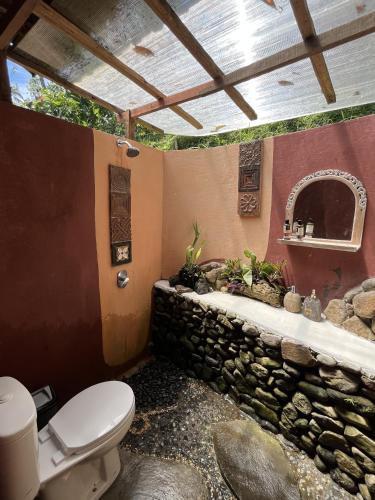 a bathroom with a toilet and a stone wall at duegoal farmhouse in Jatiluwih