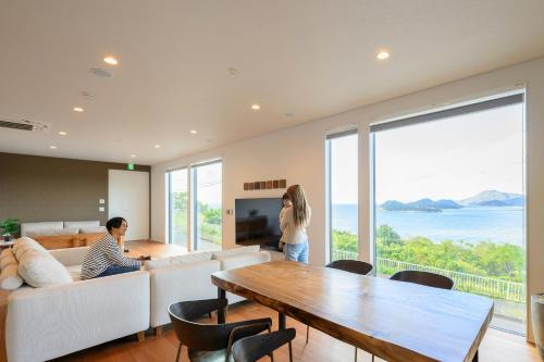 a man and woman sitting in a living room with a table at 父母ヶ浜リゾートヴィラ Senja in Mitoyo
