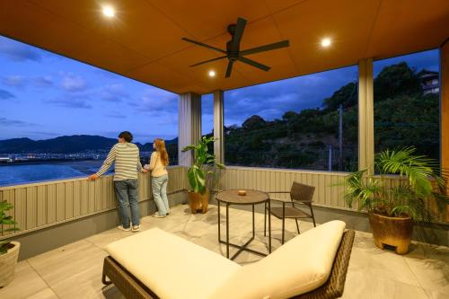 two people standing on a balcony looking out at the water at 父母ヶ浜リゾートヴィラ Senja in Mitoyo