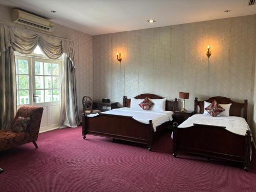 a bedroom with two beds and a chair and a window at Hidden Mansions Saigon Resort in Ho Chi Minh City
