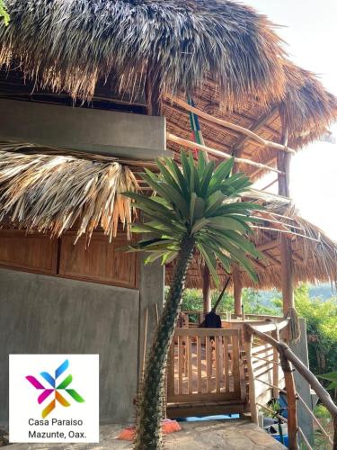 a small palm tree in front of a straw hut at Casa Paraiso Mazunte - lofts with Sea view in Mazunte