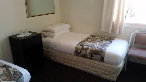 a small bedroom with a bed with a night stand and a window at Whakatane Hotel in Whakatane