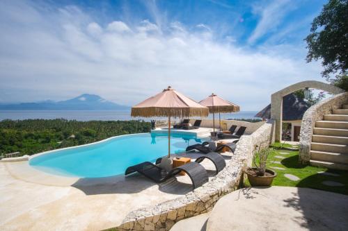 an outdoor swimming pool with chairs and umbrellas at Penida View Village - Infinity pool & Volcano View in Nusa Penida