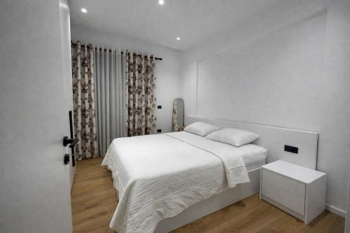 a white bedroom with a bed and a window at Dior Apartment in Vlorë