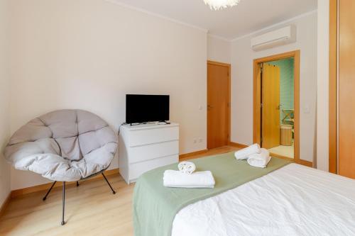 a bedroom with a bed and a chair and a television at HolidaysPT 1 - Marina Village 2 bedroom apartment in Olhão
