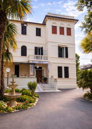 a large white building with palm trees and a fountain at Hotel Villa Pina in Senigallia
