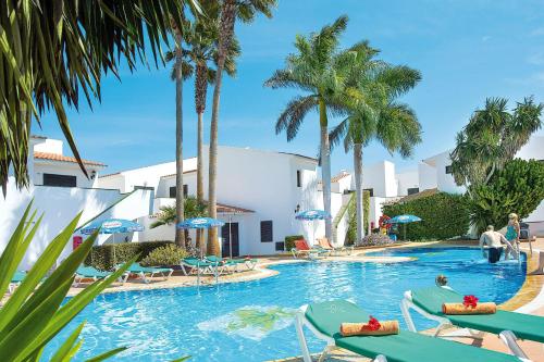 a swimming pool with chairs and palm trees at BLUESEA Puerto Caleta in Caleta De Fuste
