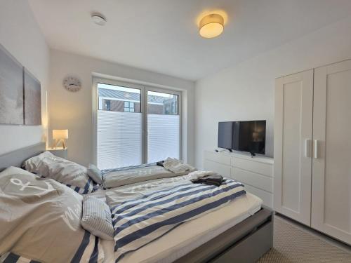 a white bedroom with a bed and a television at Ferienwohnung NordTroll in Norden