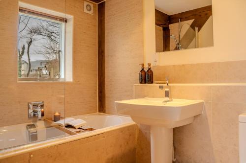 a bathroom with a sink and a bath tub at Lakeside Cotswolds Retreat with Private Hot Tub set on Lower Mill Estate in Somerford Keynes