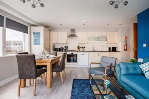 a kitchen and living room with a table and a blue couch at Seafarers - Contemporary Apartment, Central Location in Poole
