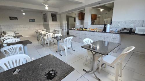 a restaurant with white chairs and tables and a kitchen at Hotel Pousada Executiva Itabuna in Itabuna
