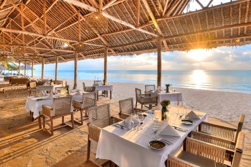 a restaurant on the beach with tables and chairs at Diamonds Leisure Beach & Golf Resort in Diani Beach