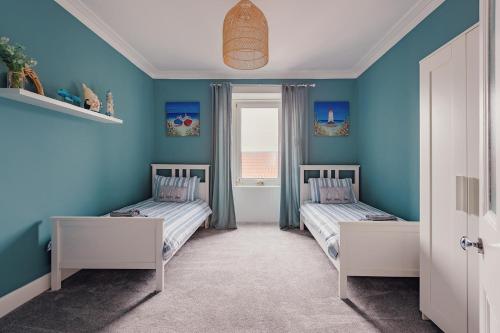 two beds in a room with blue walls and a window at The Wee Harbour Home in Anstruther