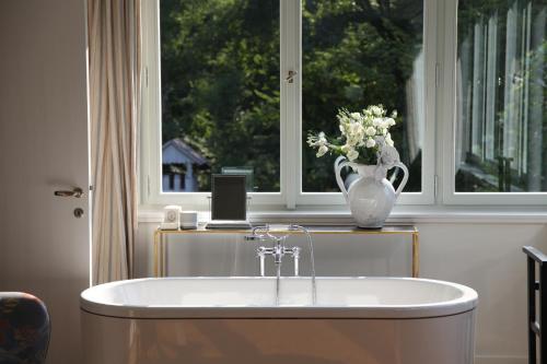 a bath tub in front of a window with a vase of flowers at Villa Čisovice - Functionalist Retreat near Prague in Čisovice