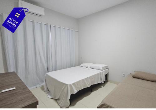 a white room with a bed and a blue sign at Casa Coqueiro 02 in Primavera do Leste