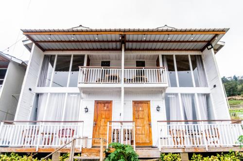 a white house with wooden doors and a balcony at Altura Cabin Dieng in Diyeng