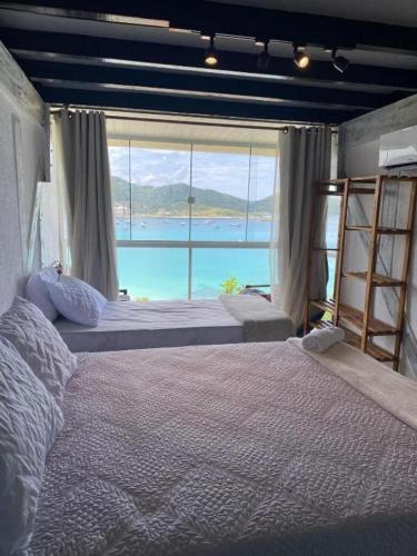 a bedroom with two beds and a large window at Pousada Mirante do Atalaia Oficial II in Arraial do Cabo