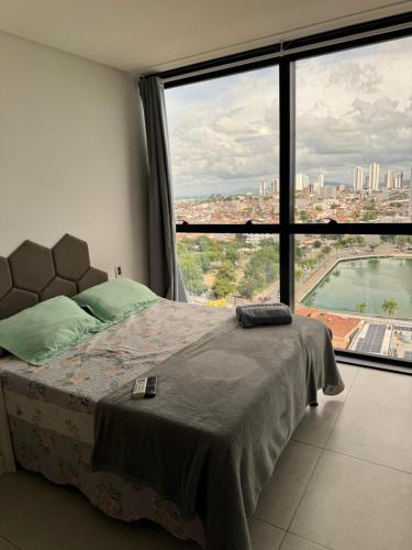 a bedroom with a bed and a large window at Flat luxo vista pro açude in Campina Grande